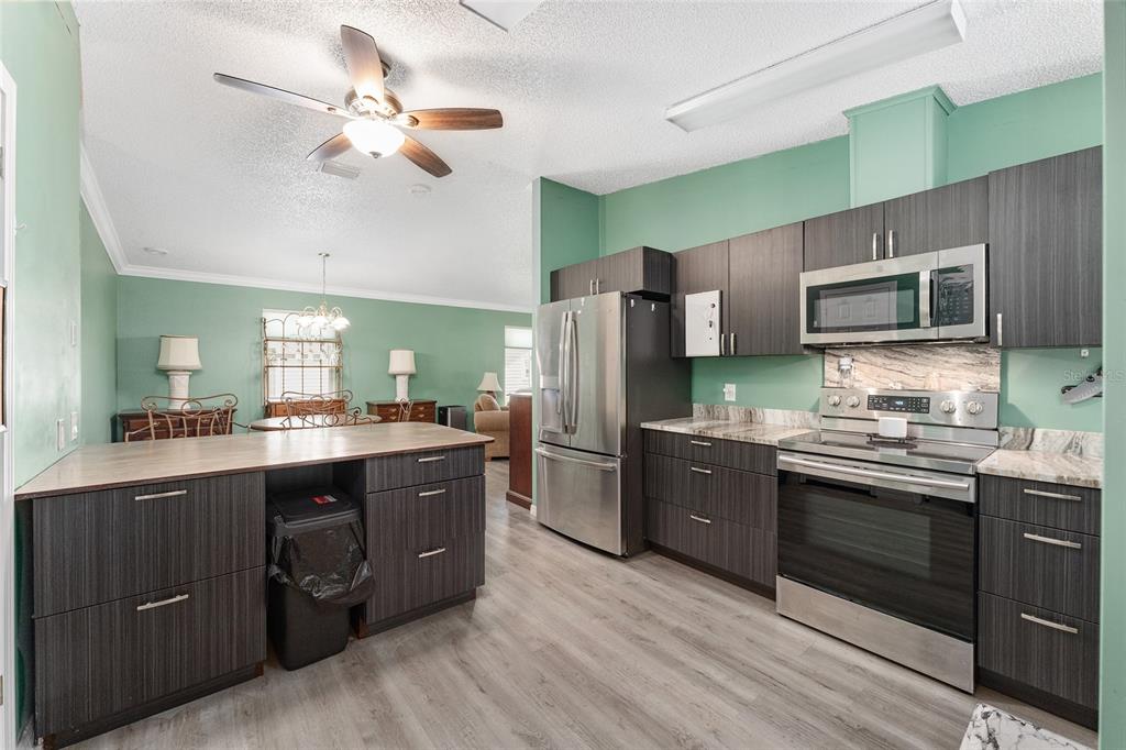 A kitchen with dark wood cabinets, stainless steel appliances, and light wood-look flooring — 1401 W SCHWARTZ BOULEVARD, LADY LAKE, FL
