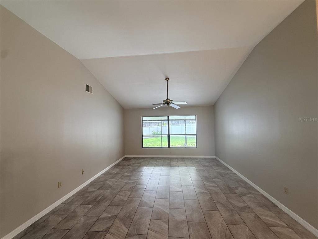A vacant room features vaulted ceilings, a ceiling fan, gray walls, and wood-look tile flooring — 18306 FELSPAR WAY, TAMPA, FL