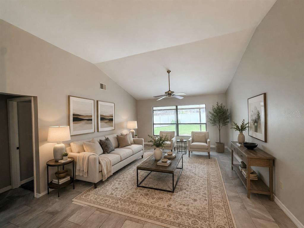 A living room with a vaulted ceiling, neutral furniture, a patterned rug, and tile flooring — 18306 FELSPAR WAY, TAMPA, FL