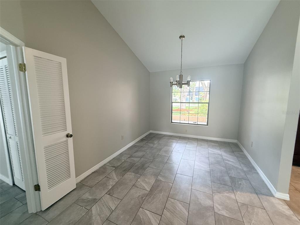 A dining room features gray tile flooring, a vaulted ceiling, and a chandelier — 18306 FELSPAR WAY, TAMPA, FL