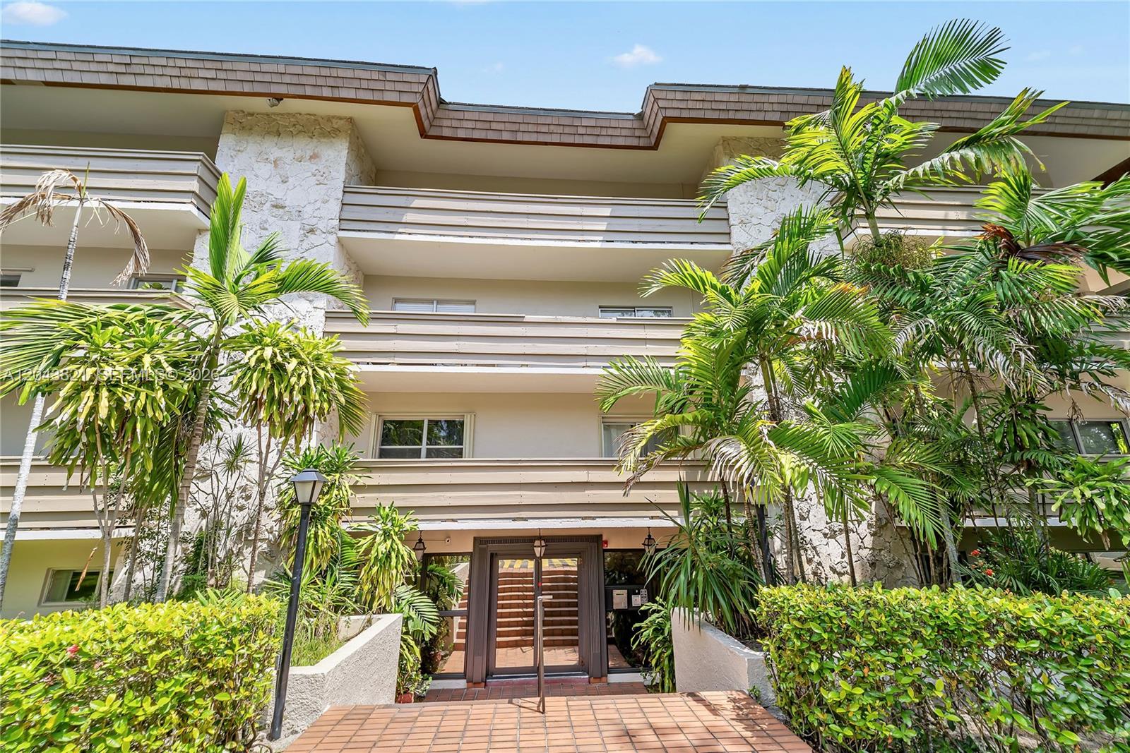 The exterior of a multi-story apartment building features stone accents, balconies, and surrounding palm trees — 1205 Mariposa Ave # 307, Coral Gables FL 33146, CORAL GABLES, FL