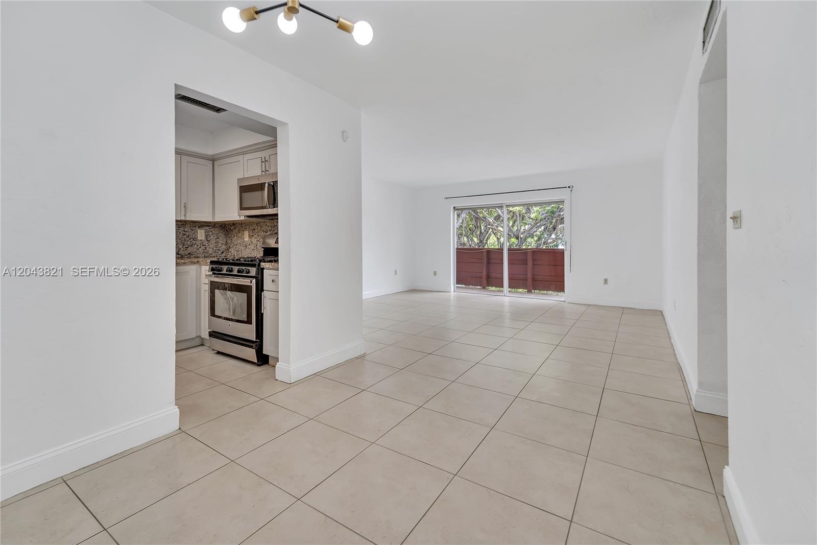 An open-concept living area with tile flooring leads to a kitchen and a sliding door — 1205 Mariposa Ave # 307, Coral Gables FL 33146, CORAL GABLES, FL