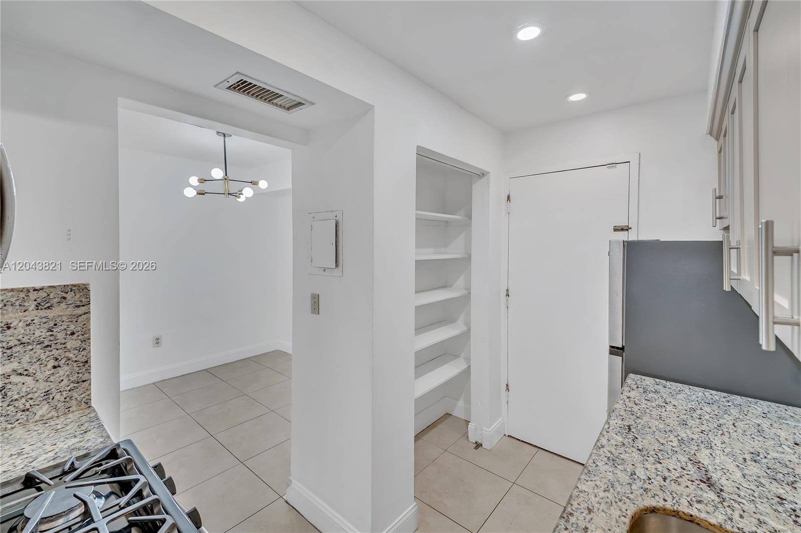 A kitchen with granite countertops and open shelving leads into a dining area — 1205 Mariposa Ave # 307, Coral Gables FL 33146, CORAL GABLES, FL