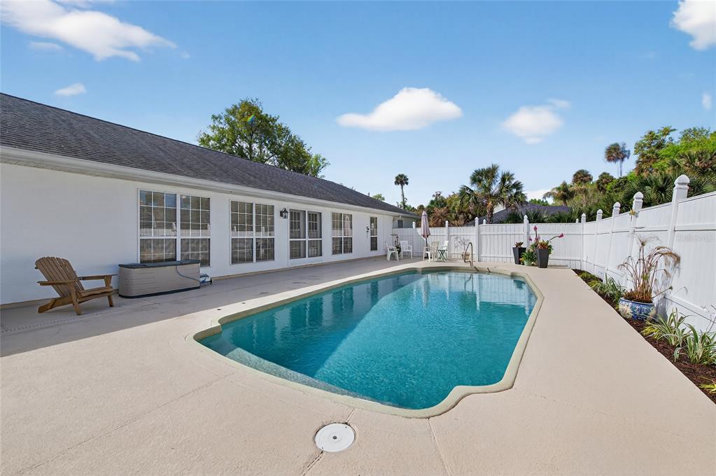 A backyard swimming pool with a concrete deck sits beside a white house and fence — 2225 JUANITA DRIVE, NEW SMYRNA BEACH, FL