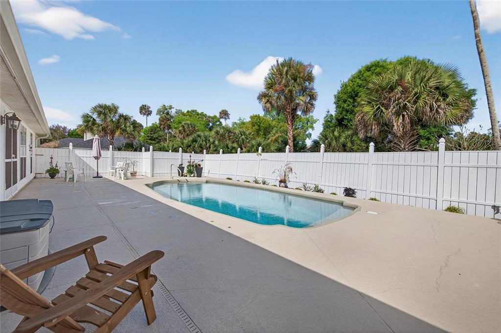 A backyard features a swimming pool, a concrete patio, and a white vinyl privacy fence — 2225 JUANITA DRIVE, NEW SMYRNA BEACH, FL