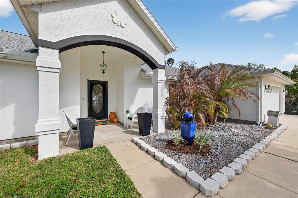The exterior of a white house features a covered entryway, a stone-bordered garden, and driveway — 2225 JUANITA DRIVE, NEW SMYRNA BEACH, FL