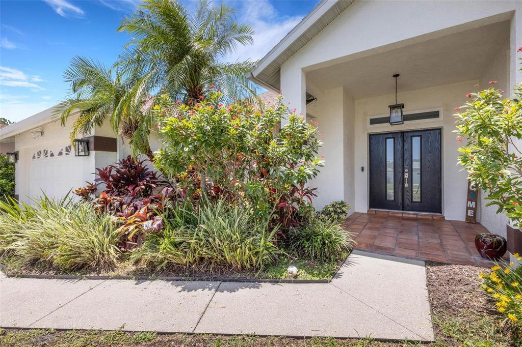 The front exterior of a house features a tiled entryway, double doors, and lush landscaping — 2426 ICECAPADE DRIVE, SARASOTA, FL