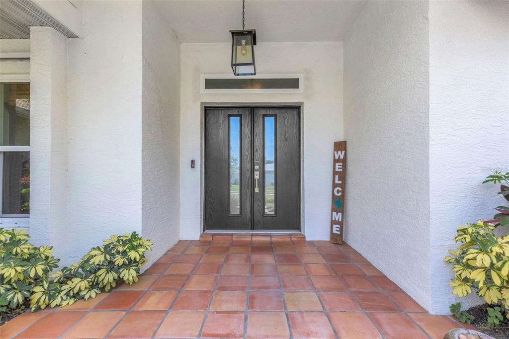 A covered entryway features a tiled floor, double front doors, and a vertical welcome sign — 2426 ICECAPADE DRIVE, SARASOTA, FL