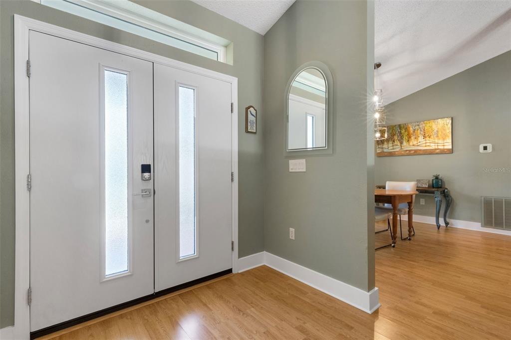 An entryway features a double front door, light wood flooring, and an arched wall mirror — 2426 ICECAPADE DRIVE, SARASOTA, FL