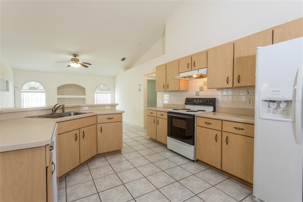 A kitchen with light wood cabinets, white appliances, and tiled floors in an open floor plan — 38 PITTWICK LANE, PALM COAST, FL