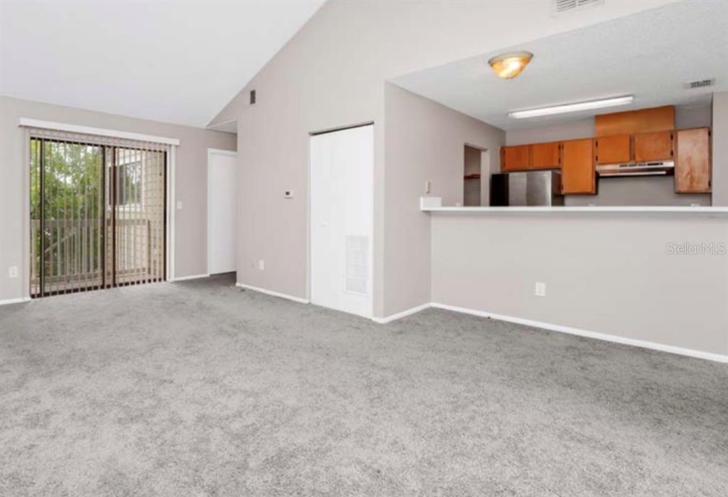 An interior view of a living room with gray carpet, vaulted ceilings, and a kitchen — 7298 ULMERTON UNIT 112, LARGO, FL