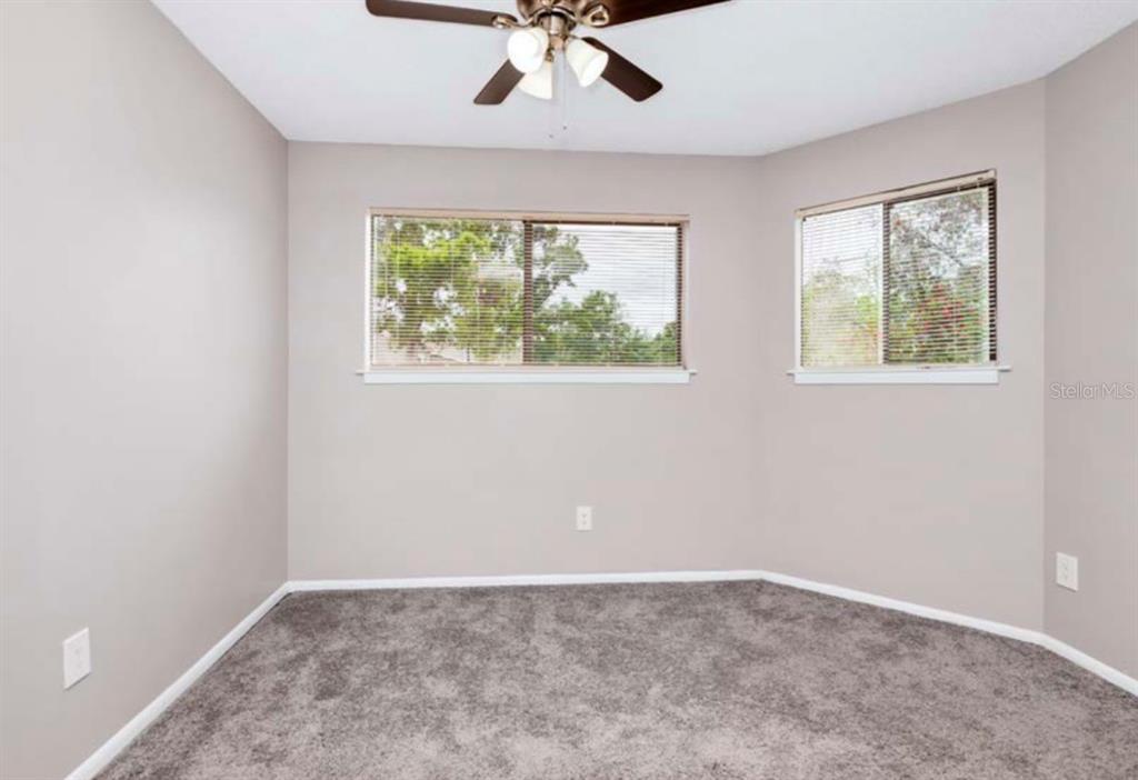 An empty bedroom features gray carpet, light-colored walls, a ceiling fan, and two windows — 7298 ULMERTON UNIT 112, LARGO, FL