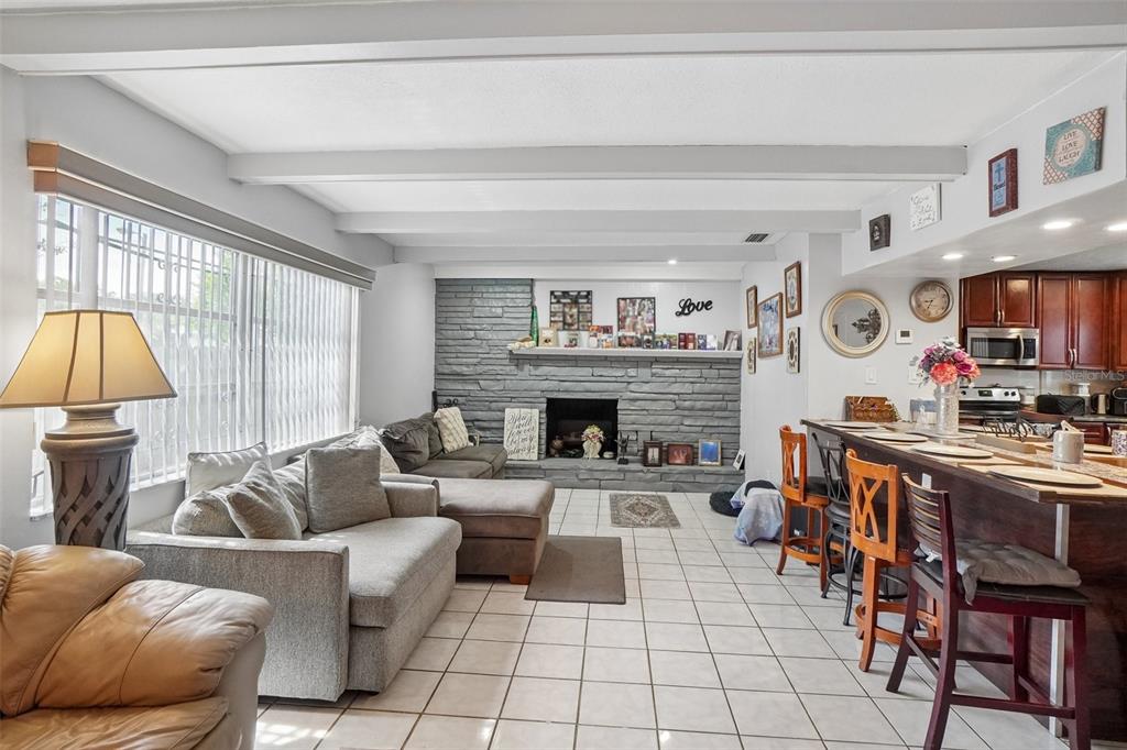 A living room with a gray stone fireplace, tiled floors, and an adjacent kitchen breakfast bar — 3495 OAK STREET, DUNEDIN, FL