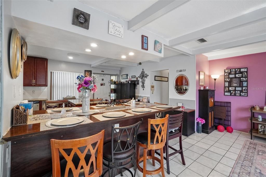 A dining area features a long wooden bar counter with stools and tiled flooring — 3495 OAK STREET, DUNEDIN, FL