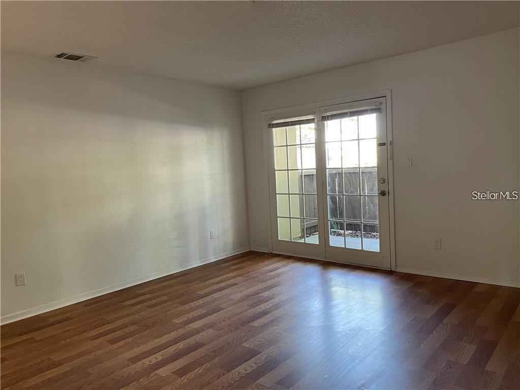 An empty room features wood-look flooring, white walls, and glass sliding doors leading outside — 246 AFTON SQUARE UNIT 105, ALTAMONTE SPRINGS, FL