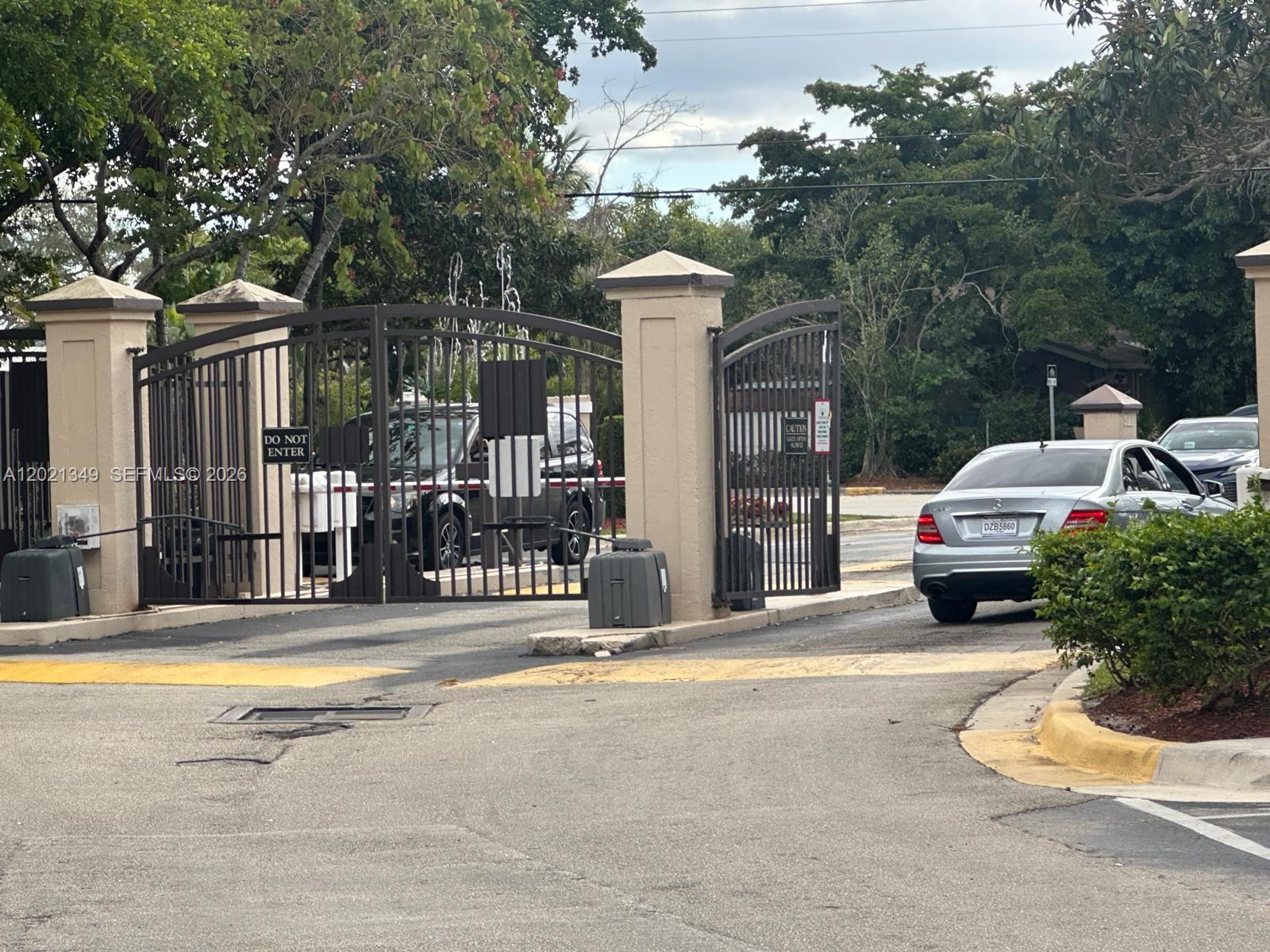 A silver car exits through an open metal gate at a residential community entrance — 4481 W Mcnab Rd # 37, Pompano Beach FL 33069, POMPANO BEACH, FL