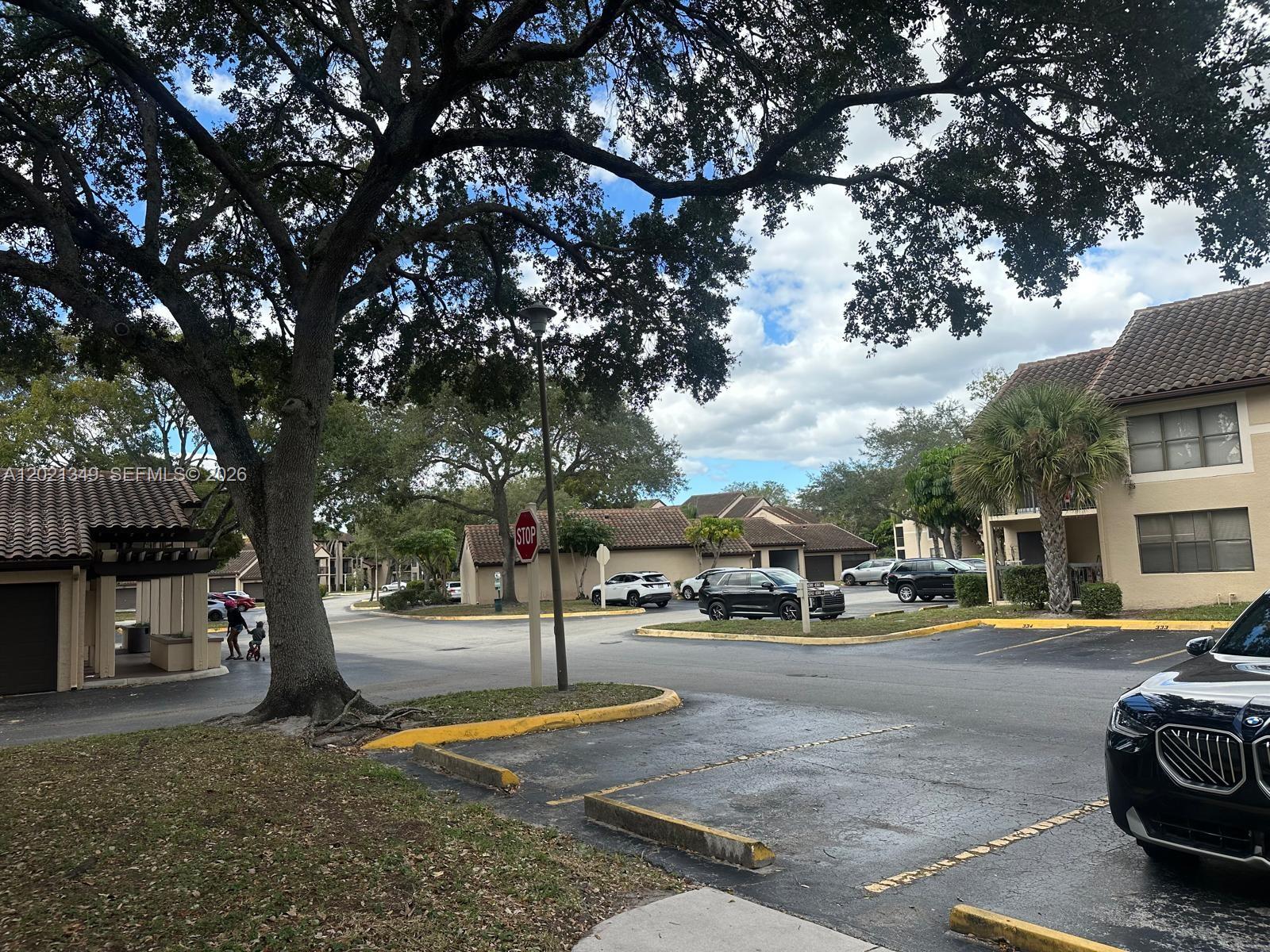 An outdoor view of a residential parking lot with trees, a stop sign, and buildings — 4481 W Mcnab Rd # 37, Pompano Beach FL 33069, POMPANO BEACH, FL