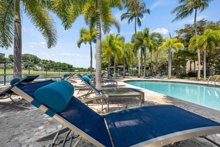 A swimming pool area features lounge chairs on a patio surrounded by palm trees — 5555 N Military Trl, Boca Raton FL 33496, BOCA RATON, FL