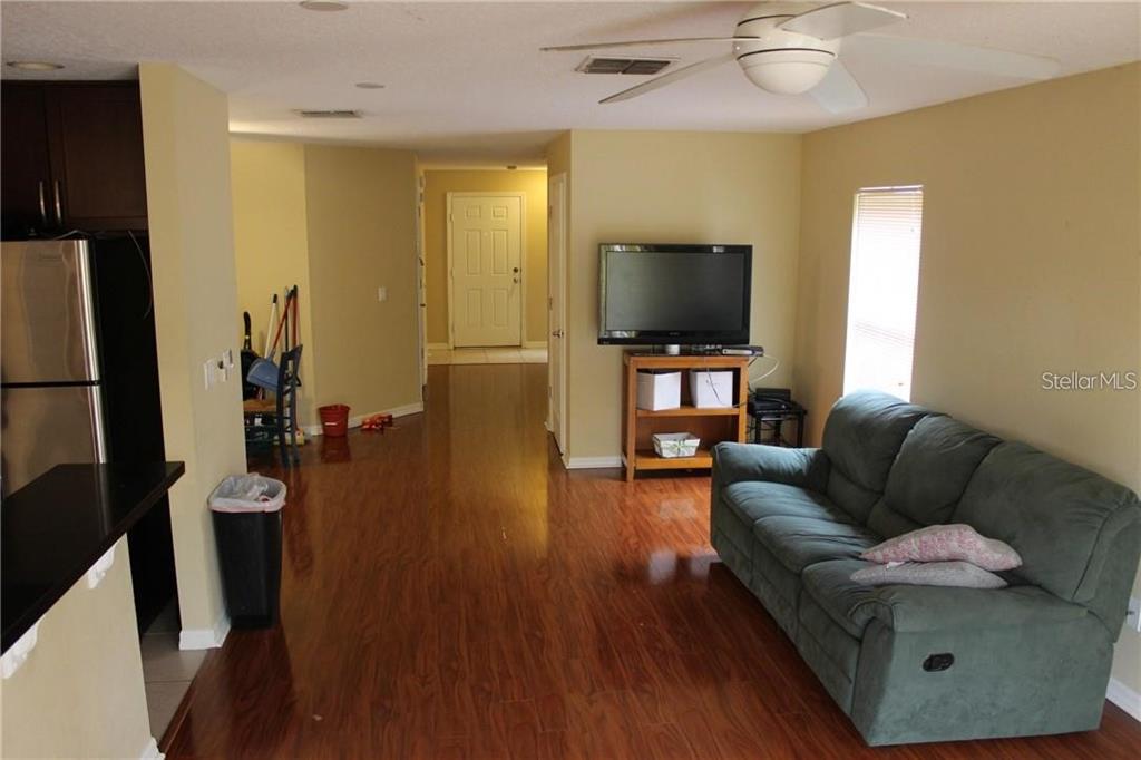 A living room with wood-look flooring, a green sofa, and a television on a stand — 4478 MAIDENHAIR COVE, OVIEDO, FL