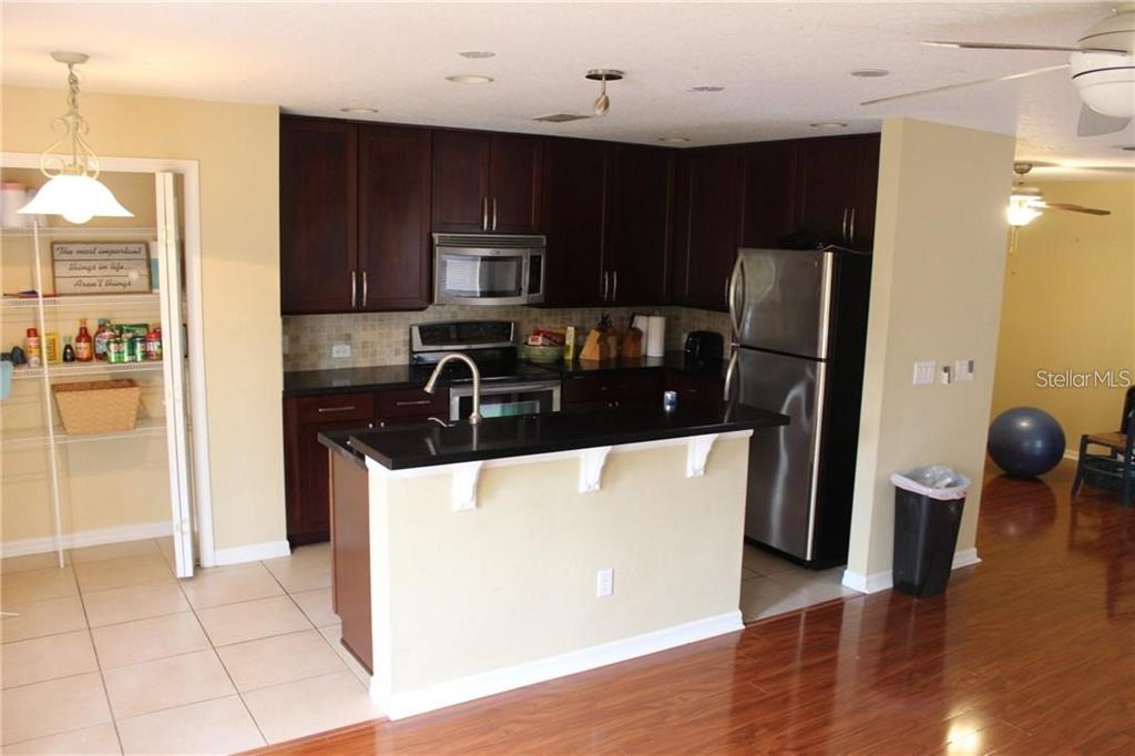 A kitchen features dark wood cabinets, black countertops, stainless steel appliances, and a breakfast bar — 4478 MAIDENHAIR COVE, OVIEDO, FL