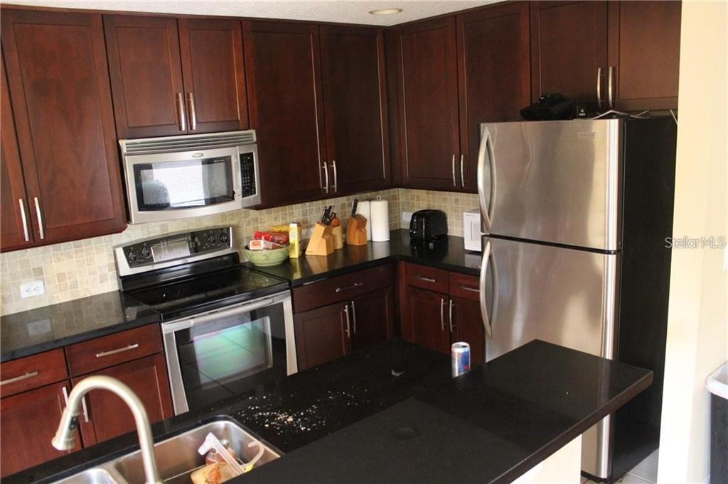 A kitchen features dark wood cabinets, black countertops, and stainless steel appliances — 4478 MAIDENHAIR COVE, OVIEDO, FL
