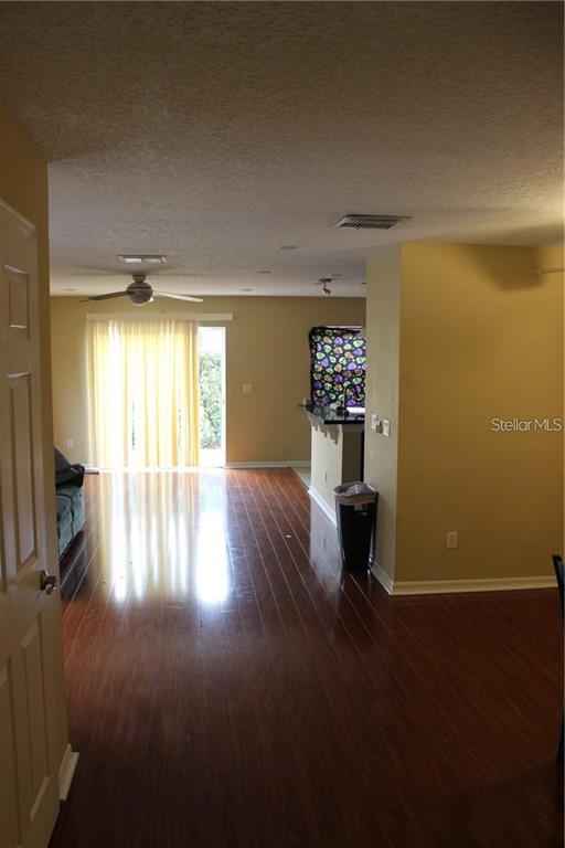 An interior view shows a living area with hardwood floors, a ceiling fan, and kitchen — 4478 MAIDENHAIR COVE, OVIEDO, FL