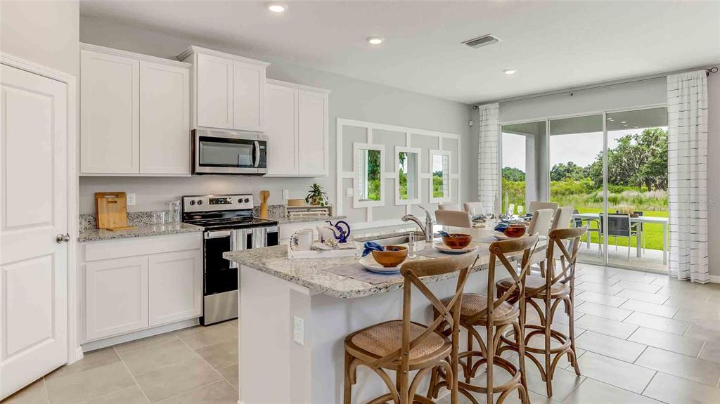 A kitchen with white cabinets, granite countertops, and a center island overlooks a dining area — 32488 ROSEPINE BOULEVARD, WESLEY CHAPEL, FL