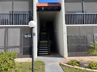 A two-story apartment building exterior features screened balconies, a central staircase, and a street lamp — 3233 BENEVA ROAD UNIT 104, SARASOTA, FL