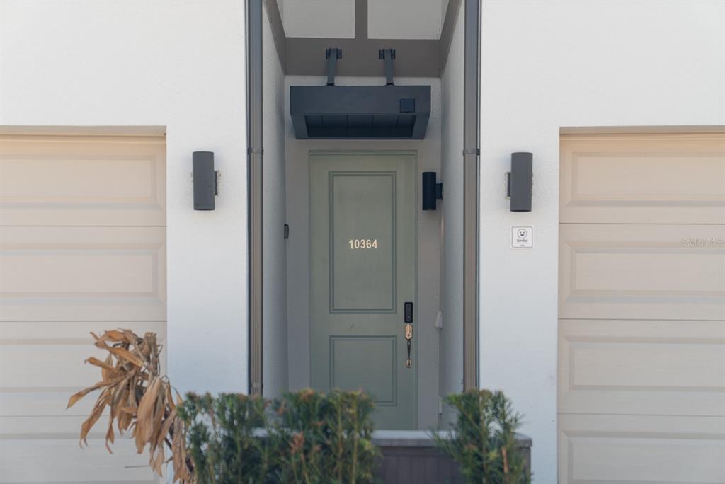 A sage green front door with the number 10364 is flanked by two beige garage doors — 10364 EBB TIDE LANE, ORLANDO, FL