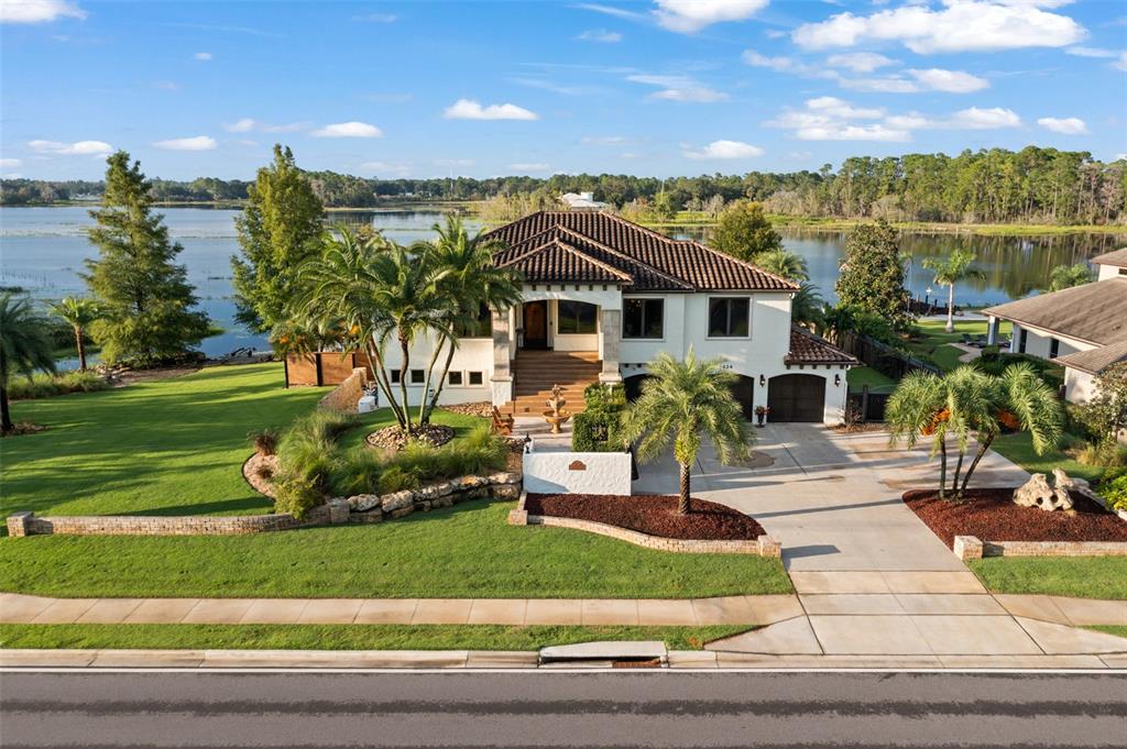 A two-story house with a tile roof sits on a lakefront lot with landscaping — 2624 HOWLAND BOULEVARD, DELTONA, FL