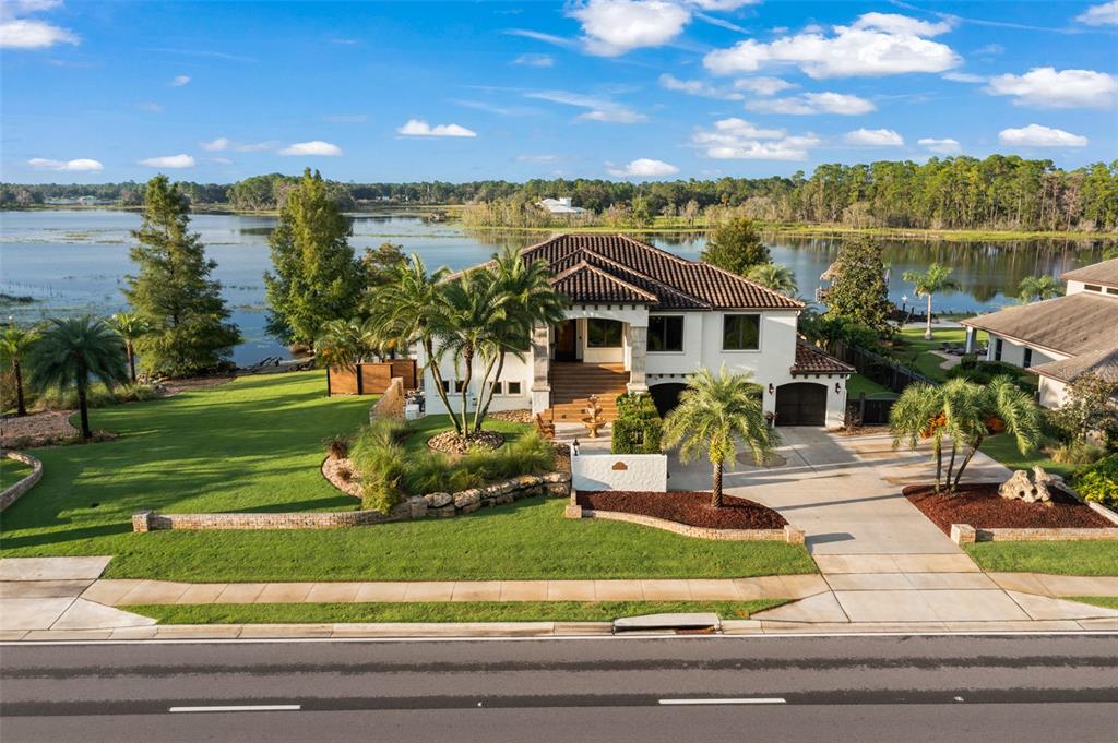 An aerial view of a two-story house with a tile roof, palm trees, and lakefront — 2624 HOWLAND BOULEVARD, DELTONA, FL