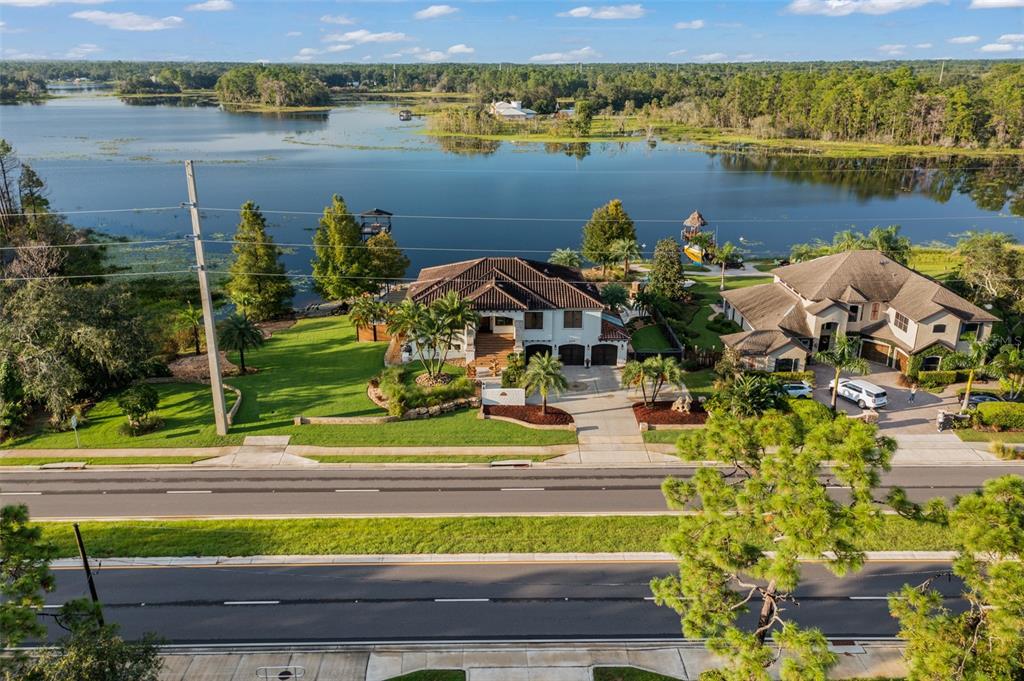 An aerial view shows two large houses situated along a lakefront with a road nearby — 2624 HOWLAND BOULEVARD, DELTONA, FL