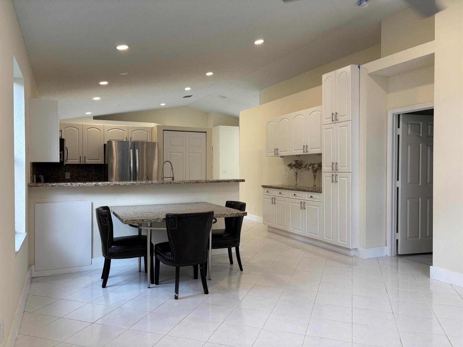 A kitchen with white cabinets, granite countertops, and a dining table with three black chairs — 9676 Cherry Blossom Court, Boynton Beach FL 33437, BOYNTON BEACH, FL