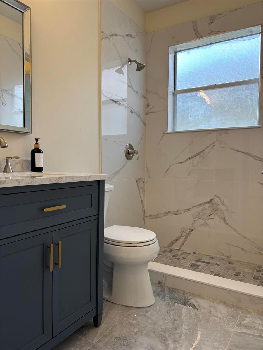 A bathroom features a dark blue vanity, marble-look wall tiles, and a walk-in shower — 9676 Cherry Blossom Court, Boynton Beach FL 33437, BOYNTON BEACH, FL