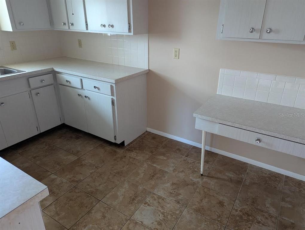 A kitchen features white cabinets, laminate countertops, a tiled backsplash, and brown tile flooring — 175 ENGLEWOOD HEIGHTS ROAD, ENGLEWOOD, FL