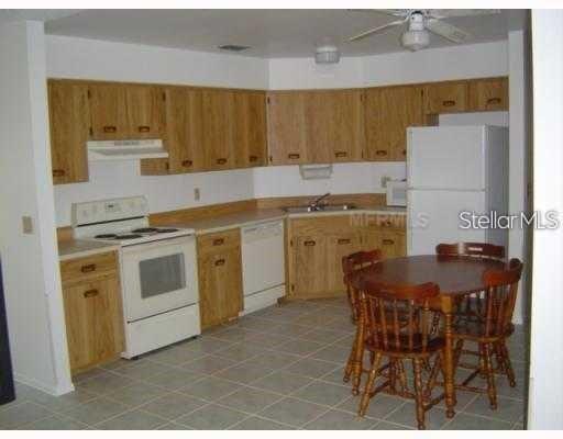 A kitchen with light wood cabinets, white appliances, and a small wooden dining table — 7681 DARCI RIDGE COURT, KISSIMMEE, FL