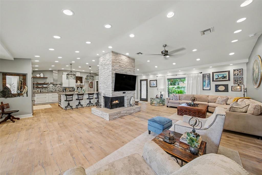 An open-concept living room and kitchen featuring a central stone fireplace and wood flooring — 30139 JOHNSONS POINT ROAD, LEESBURG, FL