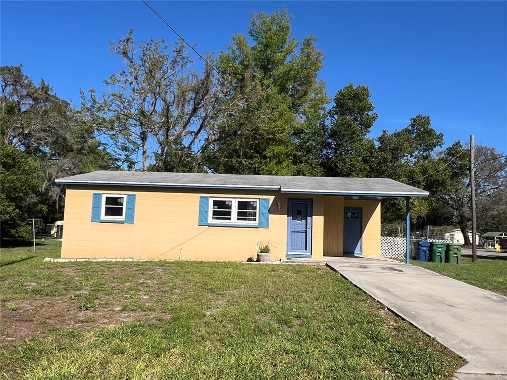 A single-story yellow house with blue shutters and a concrete driveway under a clear sky — 1602 E ANNONA AVENUE, TAMPA, FL