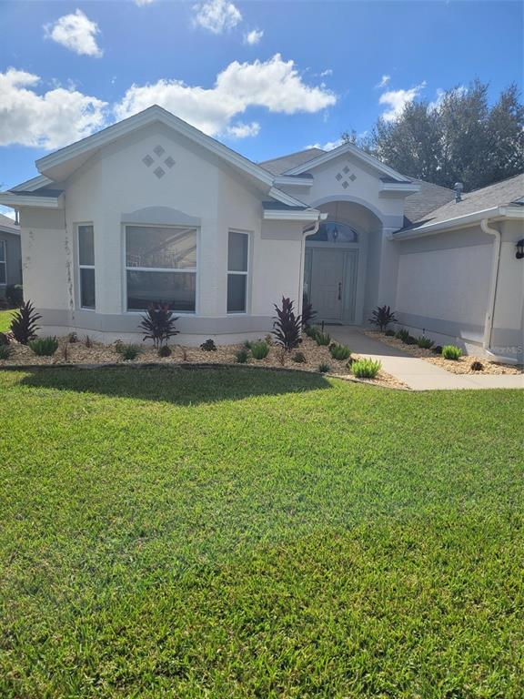 A single-story house with a light-colored stucco exterior, a front walkway, and landscaped garden beds — 3194 KEARNS CORNER, THE VILLAGES, FL