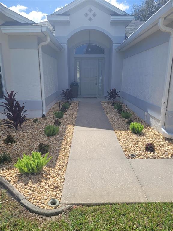 A concrete walkway leads to the front entrance of a house with light-colored stucco walls — 3194 KEARNS CORNER, THE VILLAGES, FL