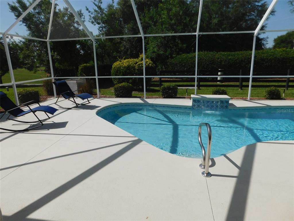 A screened-in patio features a swimming pool with a water feature and two rocking chairs — 3194 KEARNS CORNER, THE VILLAGES, FL