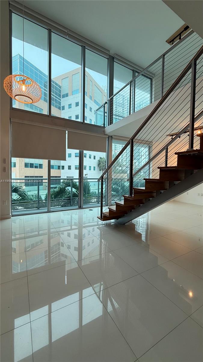 A modern living room features floor-to-ceiling windows, a floating staircase, and glossy tile flooring — 350 S Miami Ave # 302, Miami FL 33130, MIAMI, FL