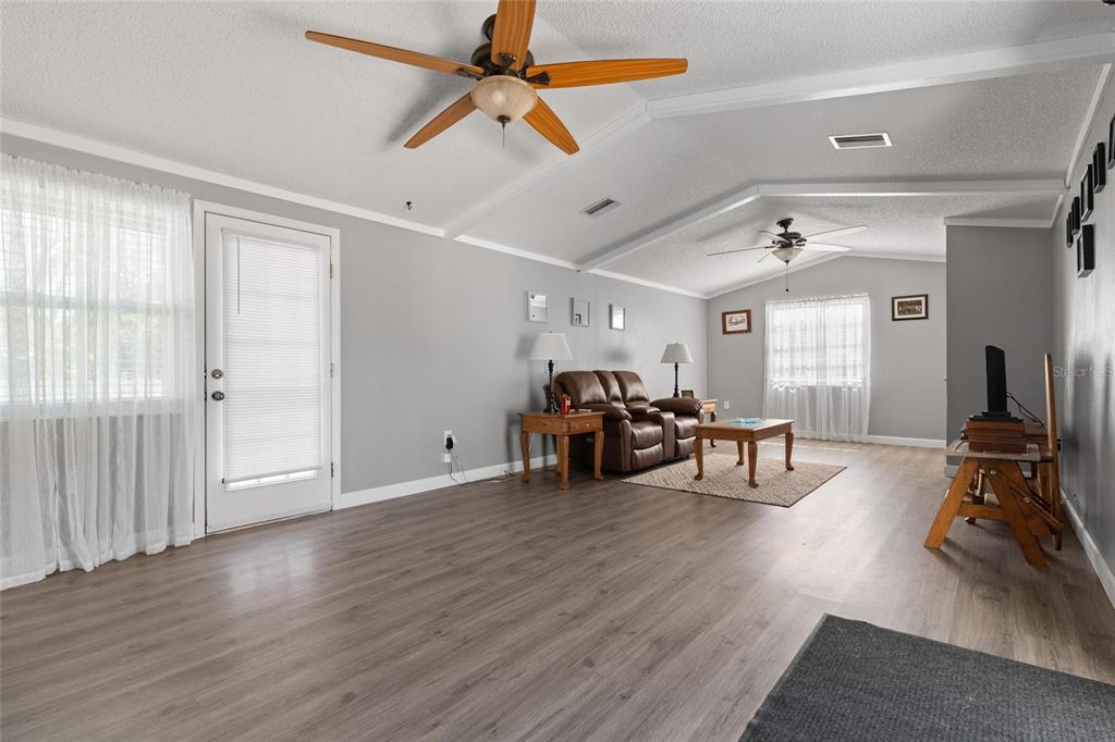 A spacious living room features light gray walls, wood-look flooring, two ceiling fans, and furniture — 5150 LIMESTONE DRIVE, PORT RICHEY, FL