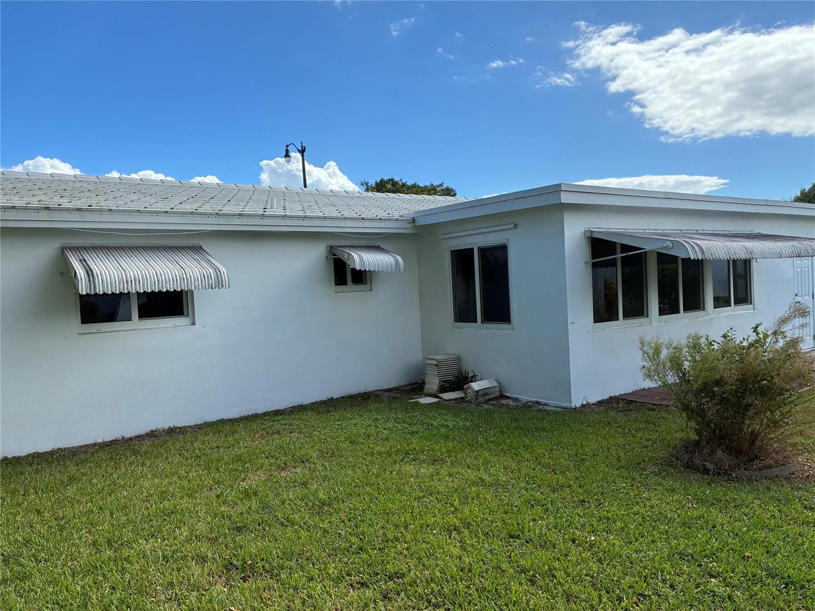 A white exterior house with striped metal awnings over the windows and a grassy yard — 3021 E Golf Boulevard, Pompano Beach FL 33064, POMPANO BEACH, FL