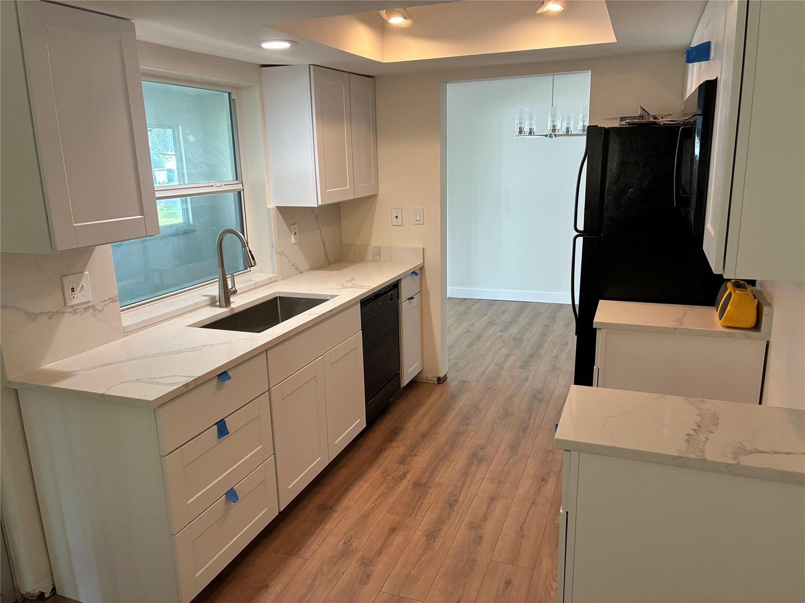 A kitchen with white cabinets, marble-look countertops, a black dishwasher, and wood-look flooring — 3021 E Golf Boulevard, Pompano Beach FL 33064, POMPANO BEACH, FL
