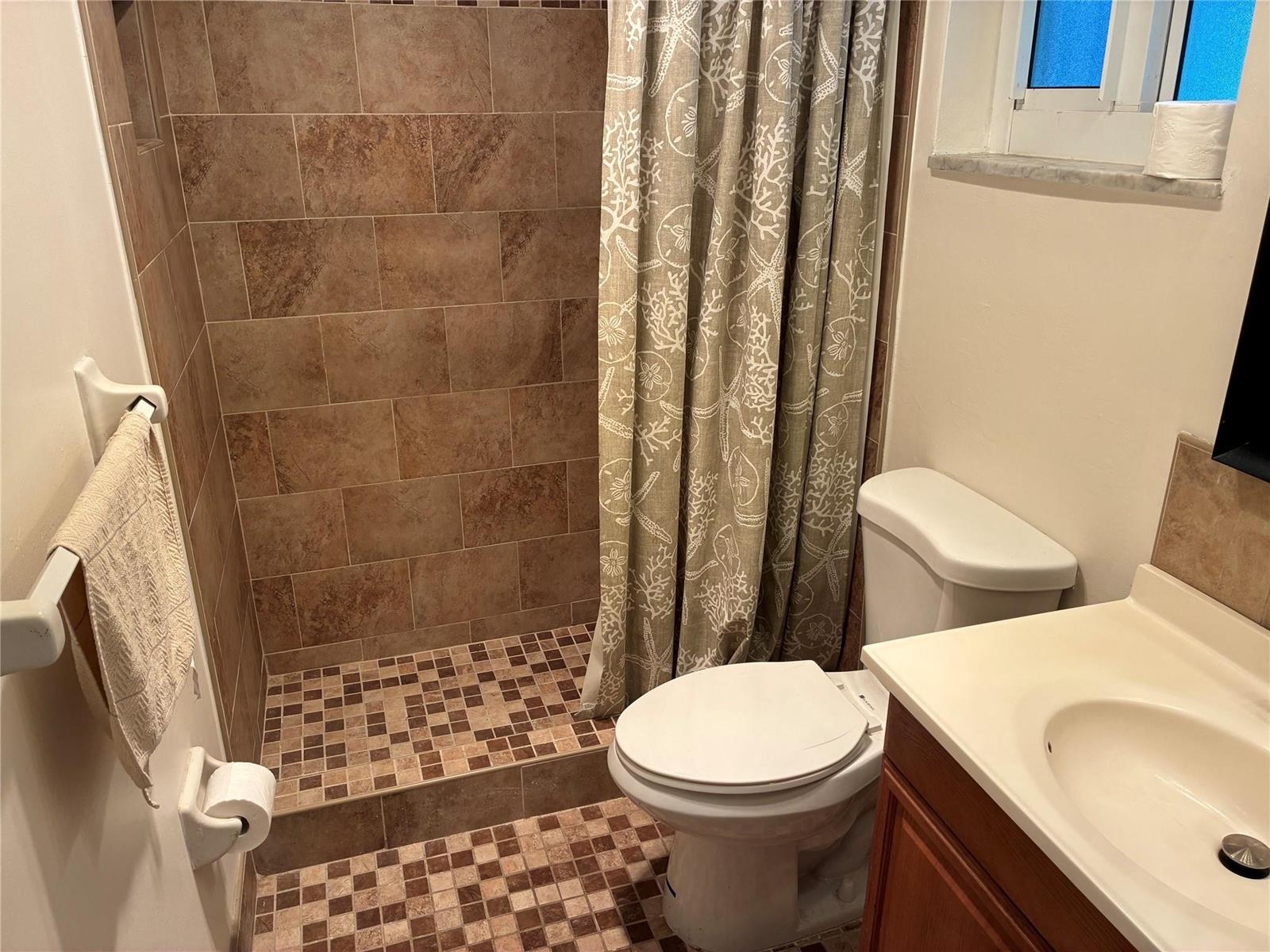 A small bathroom features a tiled walk-in shower, a toilet, and a vanity sink — 3021 E Golf Boulevard, Pompano Beach FL 33064, POMPANO BEACH, FL