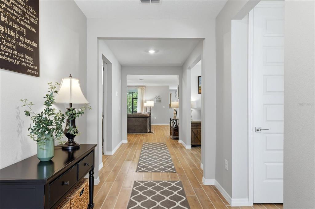 A hallway with light wood-look tile flooring leads toward an open living area — 14026 GINNIE SPRINGS WAY, PARRISH, FL