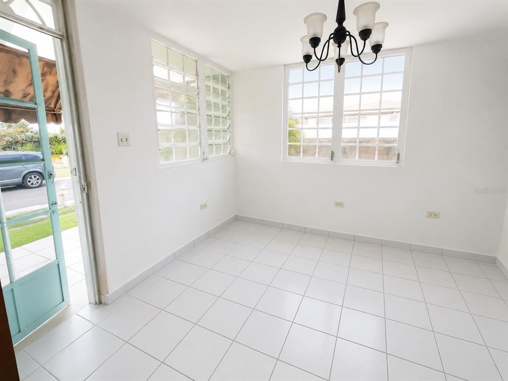 A bright dining room features white tile floors, a chandelier, and windows overlooking the street — H17 4TH STREET, ARROYO, PR