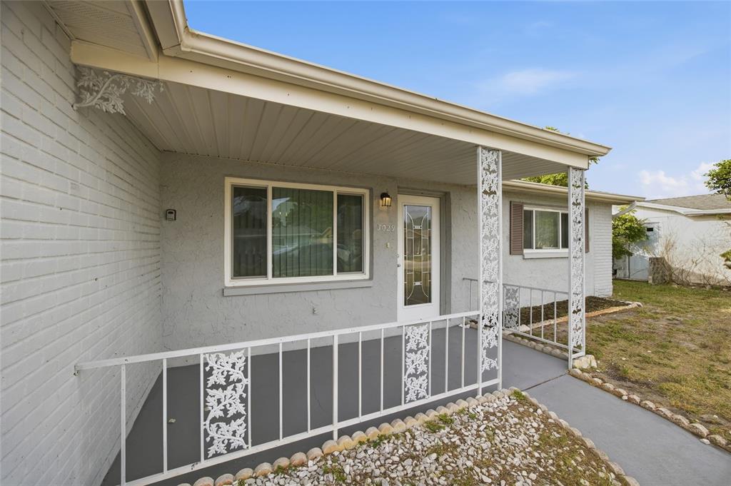 A gray house exterior features a covered front porch with white decorative metal railings — 3029 HUNTINGTON ROAD, HOLIDAY, FL