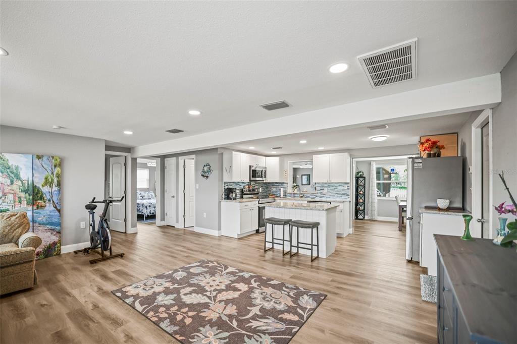 An open-concept kitchen and living area feature light wood flooring, white cabinetry, and a rug — 4704 KOALA DRIVE, HOLIDAY, FL